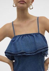 Denim vrh z tankimi spagetti naramnicami, z večplastnim ruffles designom in ravno, prilegajočo silhueto, v srednjem modrem pranju.