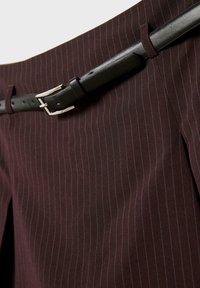 Burgundowa tkanina w prążki z czarnym skórzanym paskiem z srebrnymi elementami i klamrą, podkreślająca zdefiniowane zakładki i dopasowany krój.