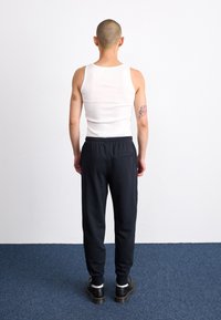 Top de tirantes blanco con textura acanalada, combinado con pantalones de chándal negros con cintura elástica y un bolsillo trasero, complementado con zapatos negros.