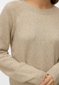 Béžový pletený svetr s kulatým výstřihem, žebrovanými manžetami a texturovanou látkou. Měkký, mírně lesklý vzhled zdůrazňující kvalitu materiálu.