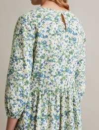 Robe fleurie avec un fond crème, présentant des motifs bleus et verts, des manches longues bouffantes, un ourlet volé et une fermeture à bouton en trou de serrure au dos.
