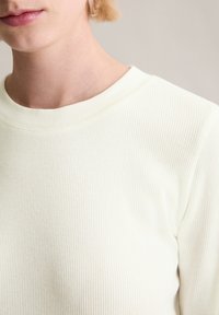 Langärmeliges, geripptes Oberteil in hellem Creme. Verfügt über einen Rundhalsausschnitt und eine weiche Textur, die Dehnbarkeit und eine figurbetonte Silhouette betont.