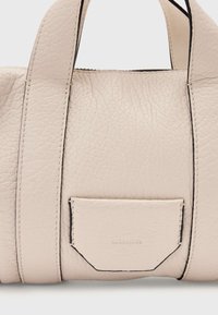 Lichtbeige leren handtas met een getextureerd oppervlak, zwarte stiksels, korte handvatten en een klein voorvak met geperst merklogo.