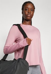 Light pink long-sleeve athletic shirt with thumbholes, paired with a black duffel bag featuring a zipper and a shoulder strap.