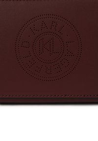 Burgundy leather wallet featuring a debossed circular logo design with perforated lettering and contrasting stitching along the edge.