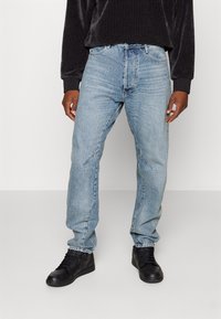 Ljusblå denimjeans med avslappnad passform, med framträdande sömmar framtill och i kombination med svarta högskaftade sneakers. Minimalistisk design.