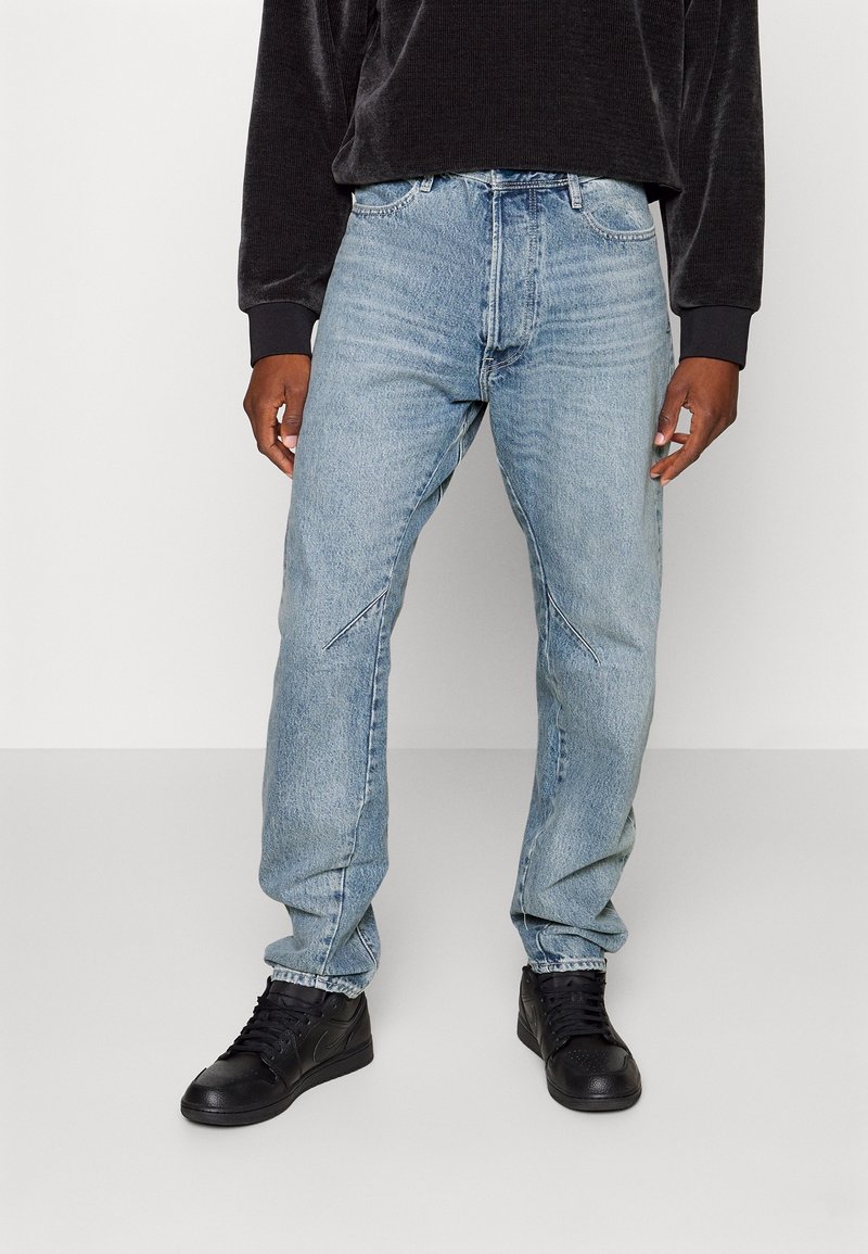 Ljusblå denimjeans med avslappnad passform, med framträdande sömmar framtill och i kombination med svarta högskaftade sneakers. Minimalistisk design.