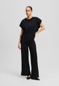 Black oversized top with floral embroidery on shoulders, paired with wide-leg black trousers featuring decorative embroidery at the hem.