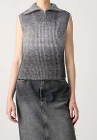 Ärmelloses graues Stricktop mit einem Frontreißverschluss und einem Ringzug, kombiniert mit einem hoch taillierten, ausgebleichten schwarzen Jeansrock.