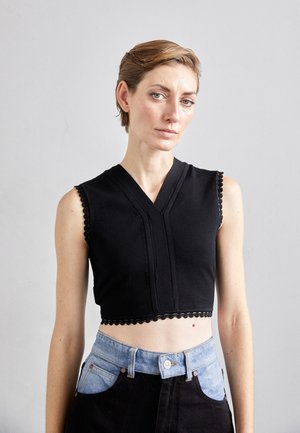 Top scurt negru cu decolteu în V, având margine decorativă ondulată și cusături orizontale. Asortat cu blugi cu talie înaltă în două tonuri.