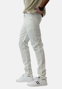 Pantaloni bianchi in cotone con una vestibilità slim, dotati di tasche anteriori e una texture liscia. Abbinati a sneakers bianche con accenti neri.
