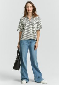 Top a maniche corte a righe in crema e blu navy, con scollo a V. Abbinato a jeans a gamba larga azzurri e sneaker bianche. Porta una borsa nera.