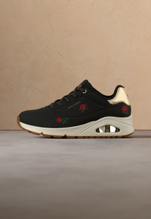 Black Skechers sneaker with red rose embroidery, beige sole with air cushion, black laces, and metallic gold heel detail.