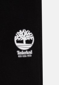 Čierna bavlnená tkanina má biele vyšívané logo Timberland so stromovým motívom a textom "Timberland N.H. USA 1973" nižšie.