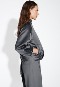 Giacca bomber in satin grigio con colletto alto, maniche a palloncino e tasche laterali. I pantaloni in un tessuto grigio abbinato presentano una vestibilità su misura.