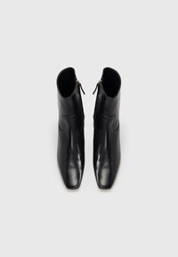 Botas de cano curto em pele preta com biqueira quadrada, fechos laterais de correr e textura lisa. Design minimalista com detalhes subtis de costura curva.