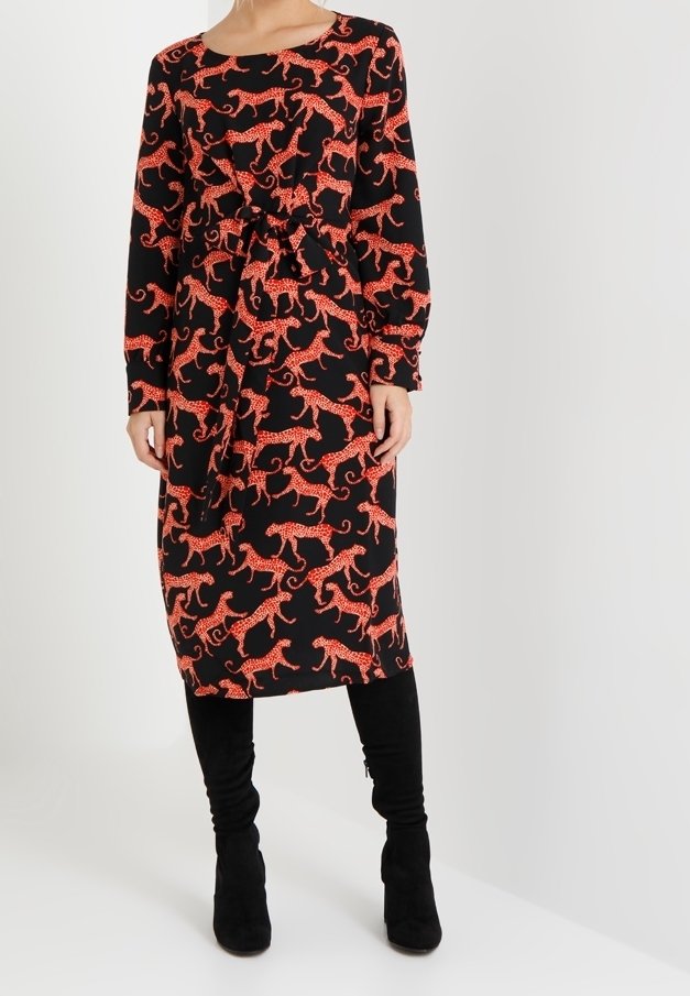 Schwarzes Kleid mit rotem Leopardenmuster, lange Ärmel, tailliert, fällt unter das Knie. Kombiniert mit schwarzen hohen Stiefeln.