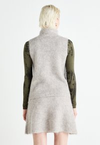 Cardigan senza maniche lavorato a maglia di grigio chiaro con un alto colletto, morbida consistenza e una silhouette svasata, abbinato a una blusa a maniche lunghe con stampa verde oliva.
