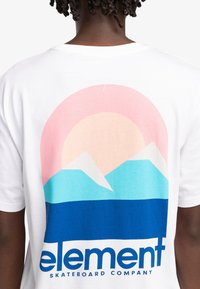 Camiseta blanca con un diseño gráfico que presenta un sol rosa, montañas azules y una franja de océano azul, con el texto "element" destacado.