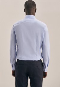 Lichtblauw overhemd met lange mouwen en een getailleerde fit, met knoopmanchetten, subtiele textuur en een klassieke kraag, gecombineerd met donkere broek.