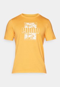Žluté bavlněné tričko s krátkými rukávy, s bílým grafickým potiskem palmových listů a nápisem "PUMA" v tučném písmu.