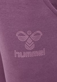Tissu violet présentant un logo texturé d'une abeille et le mot "hummel" dans un design subtil, créant un aspect cohérent.