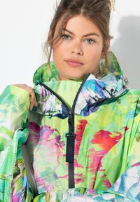 Živě zelená nepromokavá bunda s abstraktními vícolorými vzory, vysokým límcem a předním zipem s poutkem.