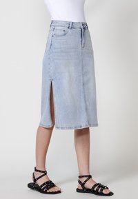 Svetlo modra denim midi krila s sprednjim razporkom, poševnim robom in zasnovo s petimi žepi. V kombinaciji s črnimi sandači na vezalko.