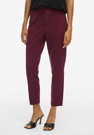 Burgundské kalhoty na míru v elegantním designu s hladkým, vysokým pasem a zúženými nohavicemi. Nosené s černými otevřenými podpatky.