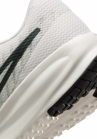 Zapatilla de correr con parte superior de malla blanca, franja verde oscuro, suela acolchada y suela exterior de goma negra con un patrón de banda de rodadura texturizado.