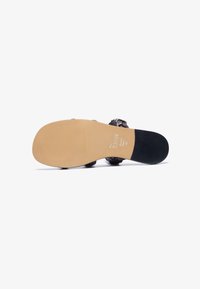 Black sandal with a textured surface, featuring a rounded toe and contoured beige sole. Brand name "ZIGN" printed on the inner sole.