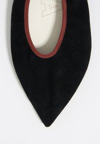 Zapato plano negro de ante con punta afilada y un ribete de tela burdeos alrededor de la abertura. Textura suave y diseño simple.