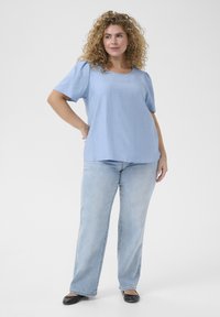 Haut à manches courtes bleu clair avec un col rond, associé à un jean en denim clair et des ballerines noires. Texture douce, coupe décontractée.