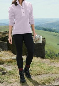 Sudadera de forro polar de color morado claro con cuello alto, botones a presión, bolsillos laterales, combinada con leggings negros y botas de senderismo negras con acentos rojos.