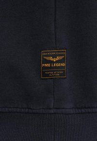 Mornarska dukserica s teksturiranim finišom, s narančastom etiketom koja glasi "PME LEGEND" i "AMERICAN CLASSIC." Ojačana rebrastim manžetama.