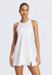 Valkoinen hihaton urheiluasu, jossa on pyöreä pääntie, rento leikkaus, sivuaukot ja sileä, kevyt kangas.