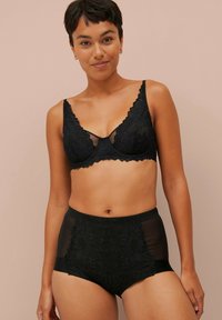 Schwarzes Lingerie-Set bestehend aus einem Spitzen-Bralette mit gewellten Kanten und passenden hochgeschnittenen Slips, beide mit transparenten Netzpaneelen.