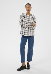 Chemise à carreaux avec manches bouffantes en crème, marine et bleu clair. Associée à un jean bleu coupe droite et des mocassins noirs.