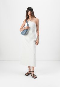 Robes maxi à rayures blanches avec des bretelles spaghetti, présentant un corsage ajusté et une jupe fluide. Associée à un sac bandoulière bleu et des sandales noires.