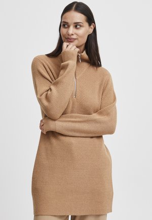 Pull en maille côtelée marron clair avec un col haut et une fermeture éclair semi-longue, arborant un motif en chevrons et des manches longues.