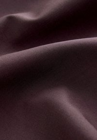 Tissu violet à la texture lisse, présentant de doux drapés et une légère brillance, dévoilant des plis subtils et une apparence uniforme.