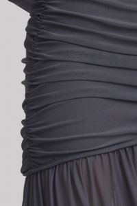 Sötétszürke ruha, fodros anyagtextúrával, sima testrésszel, amely egy könnyed, félig átlátszó szoknyába torkollik. Hangsúlyos rétegezett részletek.