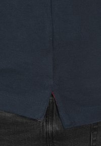 Mørkeblå polo-shirt med en struktureret stof, der har en sideslids og en kontrasterende rød accent ved kanten. Egnet til afslappet brug.