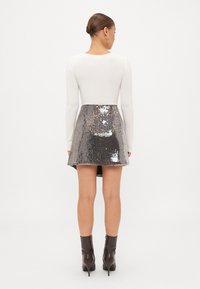 Valge pika varrukaga topp, mis on kombineeritud hõbeda sequins mini seeliku ja flared hemiga. Seelikul on peen tagumine lõige. Mustad pahkluu saapad lõpetavad välimuse.