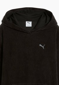 Felpa in corduroy nera con una prominente tasca a forma di canguro, texture a costine e logo argentato nella zona sinistra del petto.