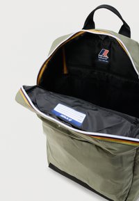 Ελιά πράσινο σακίδιο με μαύρο εσωτερικό, ανοιχτό φερμουάρ στο κύριο διαμέρισμα και ετικέτα K-Way με όνομα εσωτερικά.