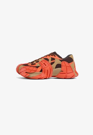 El zapato presenta una combinación de malla marrón oscuro y acentos de goma naranja, con un diseño poco convencional y una suela texturizada para mayor tracción.