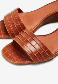 Sandales marron à bout ouvert avec trois brides texturées à motif crocodile et une semelle plate sur fond blanc.