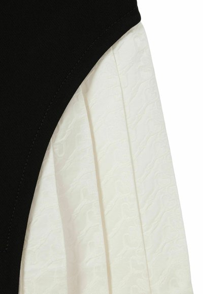 Garbata nera con un dettaglio plissettato bianco testurizzato. Il materiale presenta un motivo sottile, mentre le cuciture sono visibili sulla sezione nera.