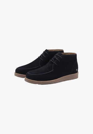 Botas de tobillo de ante negro con punta redondeada, diseño con cordones, costuras en contraste y una suela de goma marrón claro.